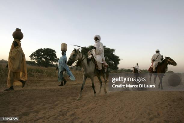 After an attack on their village forced them to flee, Arab nomads on horses pass by a Chadian village woman as they came back from a water well and...