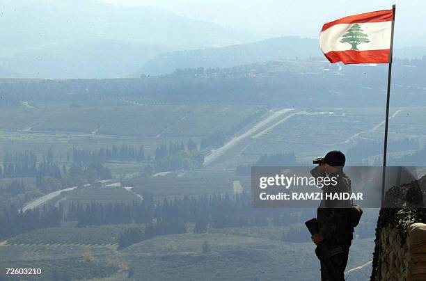 Marun Al-Ras, LEBANON: A Lebanese flag flutters as a Lebanese army soldier looks through his binoculars as he stands guard along the Lebanese-Israeli...