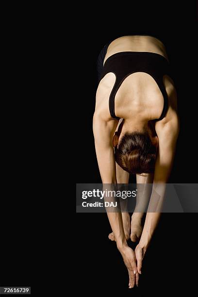 woman bending over, stretching, front view, black background, copy space - japanese ethnicity the human body stock pictures, royalty-free photos & images
