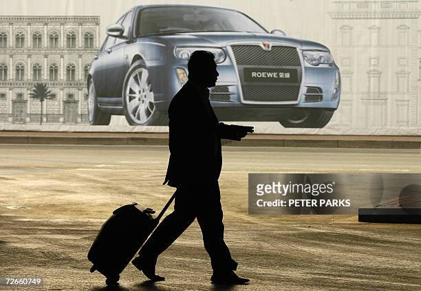 Passenger passes infront of an advertisement for the Chinese-made Roewe 750 car at Beijing's Capital airport 21 November 2006. The luxury model car...