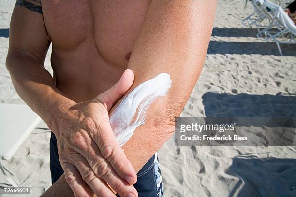 man standing on beach and applying sun cream to arm - arm sun beach stock-fotos und bilder
