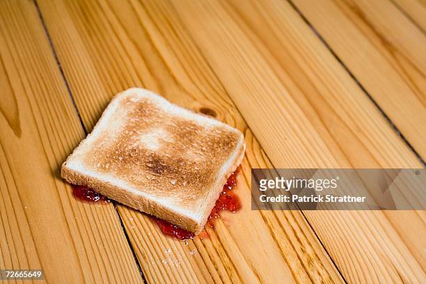 slice of toast with strawberry jam turned upside down on floor - unbequemlichkeit stock-fotos und bilder