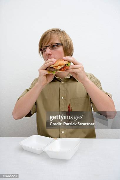 young man spilling ketchup on his shirt whilst eating a hamburger - food stain stock-fotos und bilder