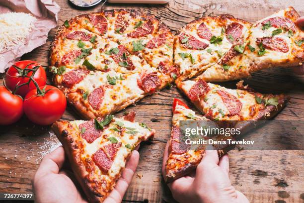 hands pulling slices of heart-shaped pizza near ingredients on cutting board - heart shape pizza stock pictures, royalty-free photos & images