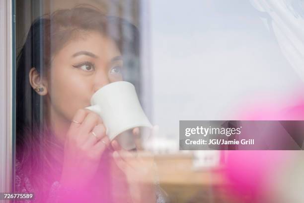 mixed race woman drinking coffee behind window - mixed race woman drinking tea stock-fotos und bilder