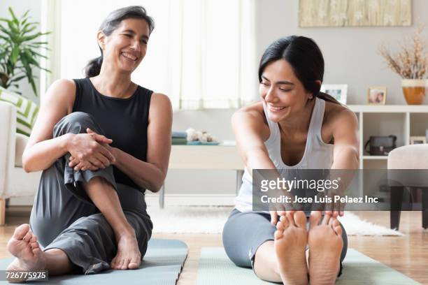mother and daughter sitting on exercise mats and stretching - mid adult women photos et images de collection