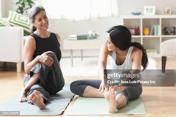 mother and daughter sitting on exercise mats and stretching legs - latina legs stock-fotos und bilder