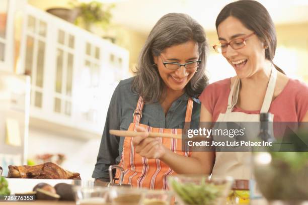 mother watching daughter cooking in domestic kitchen - indian mother and daughter stockfoto's en -beelden