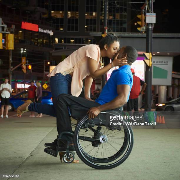 African America woman kissing man in wheelchair in city at night