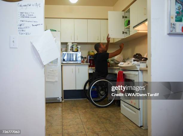 african american man in wheelchair opening cabinet in domestic kitchen - domestic life imagens e fotografias de stock