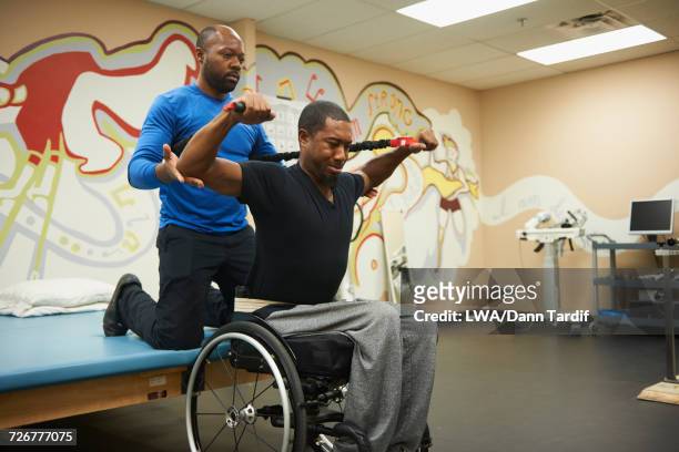Physical therapist helping man in wheelchair strengthen arms