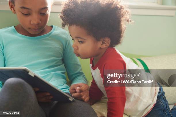 Black baby boy watching sister using digital tablet