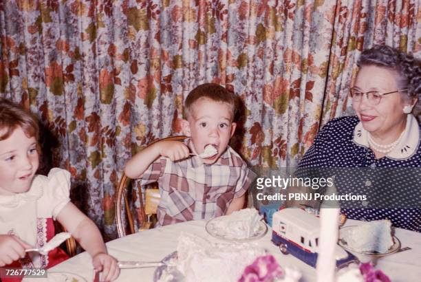 caucasian woman watching grandson and granddaughter eating cake - archival stock-fotos und bilder