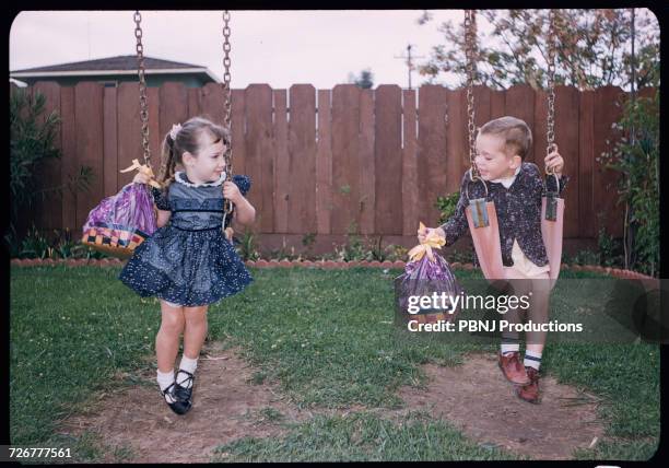 caucasian brother and sister on swings holding easter baskets - 1950 1959 mode stock-fotos und bilder