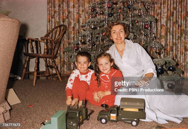 caucasian mother posing with son and daughter near christmas tree - christmas tradition stock pictures, royalty-free photos & images