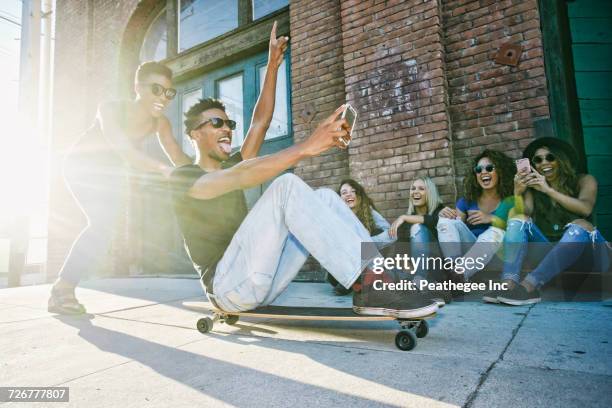 woman pushing friend sitting on skateboard in city - arab people laugh stock-fotos und bilder