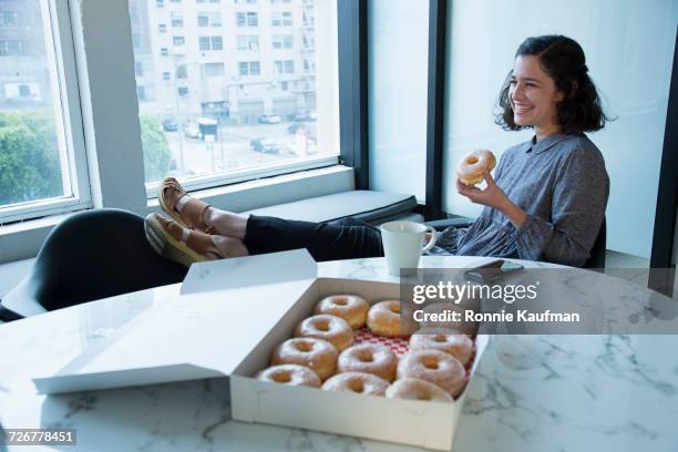 businesswoman eating donut in conference room - eating donuts foto e immagini stock