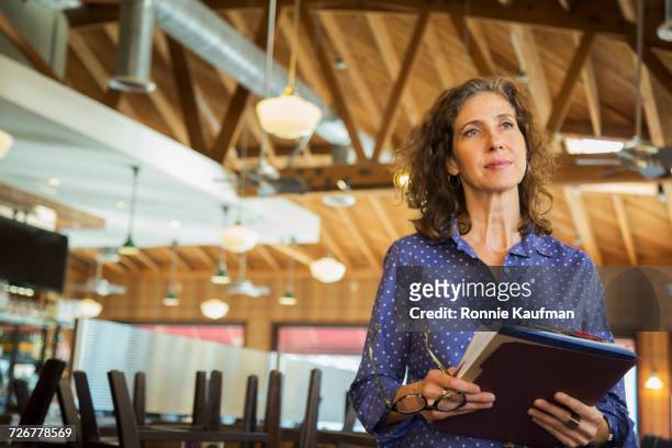 pensive caucasian woman holding paperwork in restaurant - candid curly hair stock pictures, royalty-free photos & images