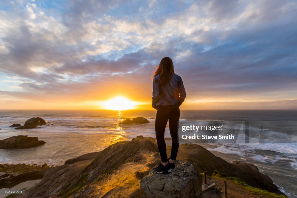 Caucasian woman standing on rock near ocean at sunset