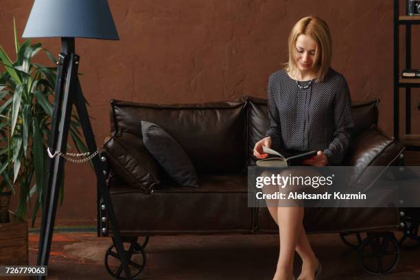 middle eastern woman sitting on sofa reading book - arab businesswoman with books stock-fotos und bilder