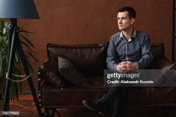 pensive middle eastern man sitting on sofa - tripod lamp stock pictures, royalty-free photos & images