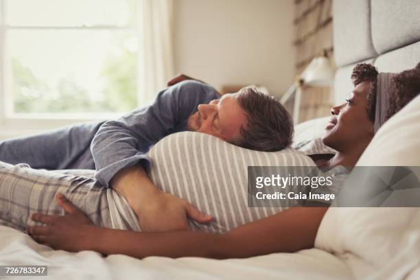 husband cuddling pregnant wife on bed - couple cuddling in bed stock pictures, royalty-free photos & images