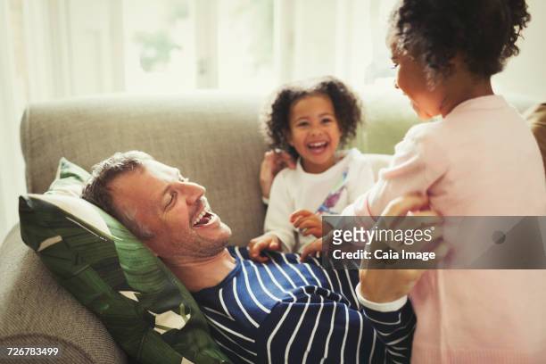 Playful multi-ethnic father and daughters tickling and laughing on sofa