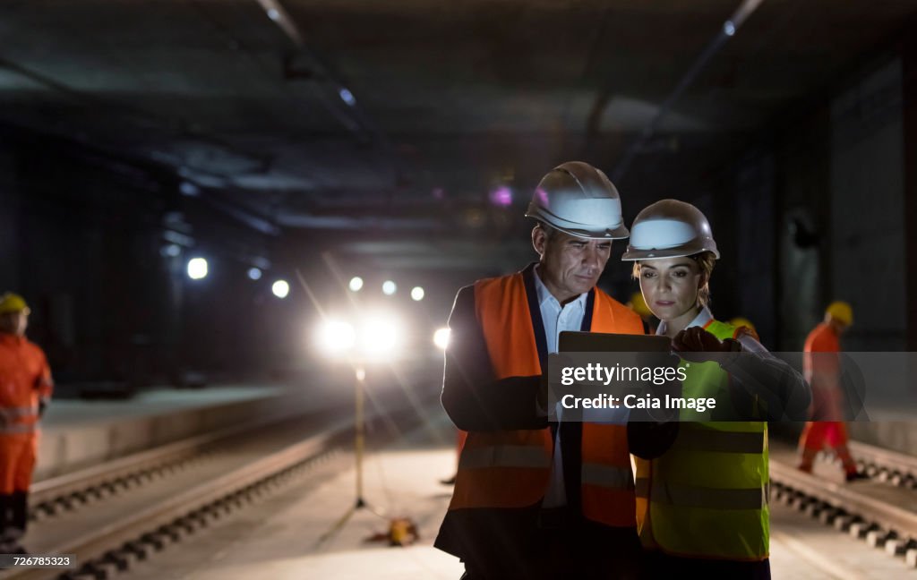 Foreman and construction worker using digital tablet at dark underground construction site
