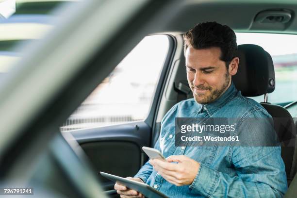 businessman sitting in car using smartphone and digital tablet - passenger seat foto e immagini stock