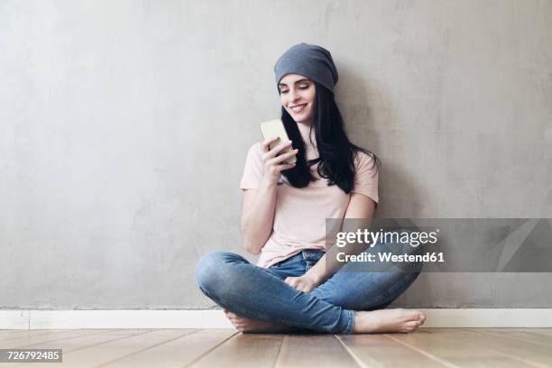 smiling young woman sitting on the floor using cell phone - fashion woman floor cross legged stock pictures, royalty-free photos & images