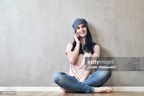 smiling young woman sitting on the floor talking on cell phone - fashion woman floor cross legged fotografías e imágenes de stock