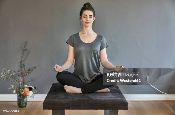 young woman sitting on lounge doing yoga - lotuspositie stockfoto's en -beelden
