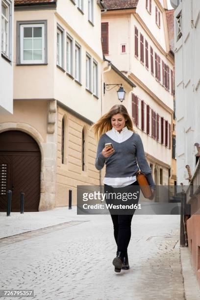 germany, tuebingen, smiling young student looking at cell phone while walking - tübingen stock pictures, royalty-free photos & images