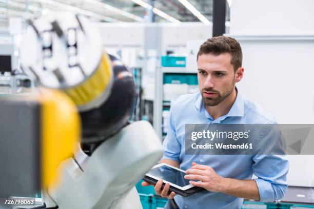 man with tablet examining assembly robot in factory shop floor - roboter industrie stock-fotos und bilder