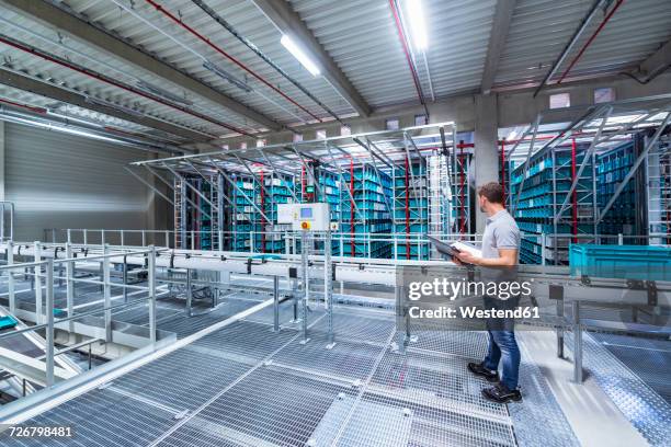 man with documents in automatized high rack warehouse - automated warehouse stock-fotos und bilder