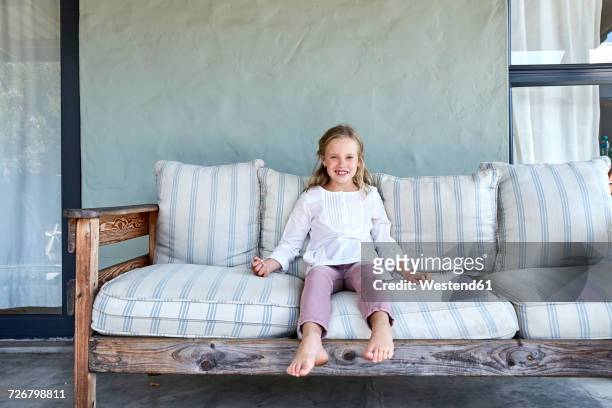 portrait of smiling blond little girl sitting on couch oo the terrace - beautiful barefoot girls imagens e fotografias de stock