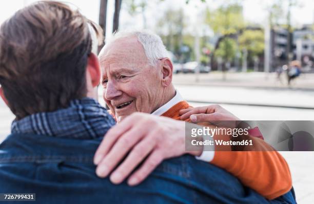 smiling senior man looking at adult grandson outdoors - reliable fotografías e imágenes de stock
