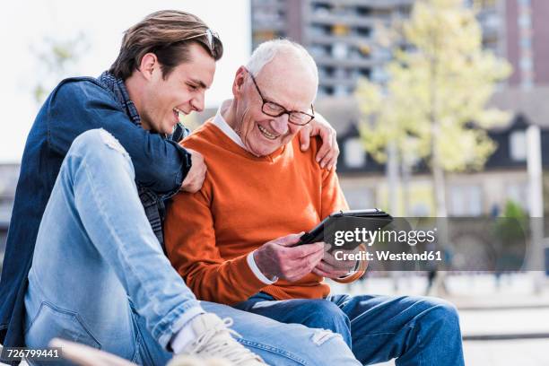 happy senior man and adult grandson looking at tablet - young at heart stock-fotos und bilder