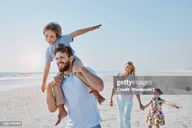 happy family strolling on the beach - llevar al hombro fotografías e imágenes de stock