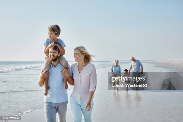 happy extended family strolling on the beach - grandma son stock pictures, royalty-free photos & images