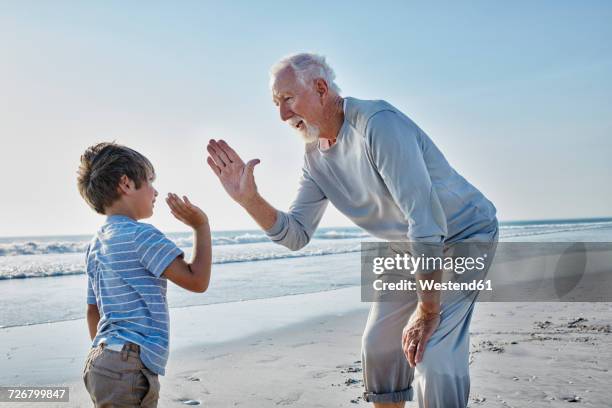 grandfather and grandson high fiving on the beach - idol photos et images de collection
