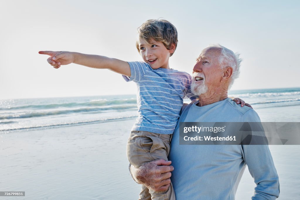 Grandfather carrying grandson on the beach