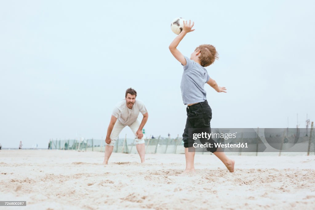 Father and little son playing with ball on the beach