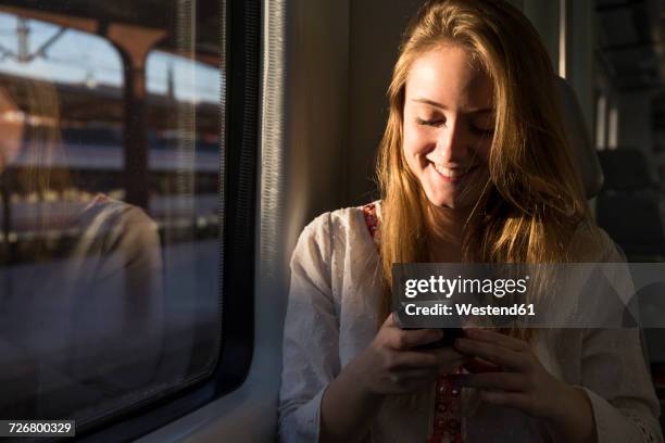 smiling young woman on a train looking at cell phone - riding hat stock-fotos und bilder