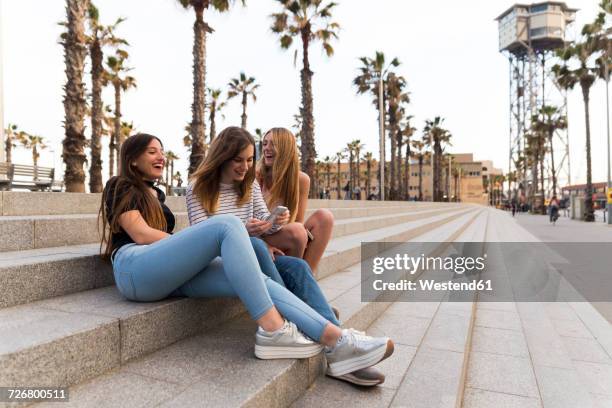 spain, barcelona, three happy young women sitting on stairs having fun - man stairs sitting stock-fotos und bilder