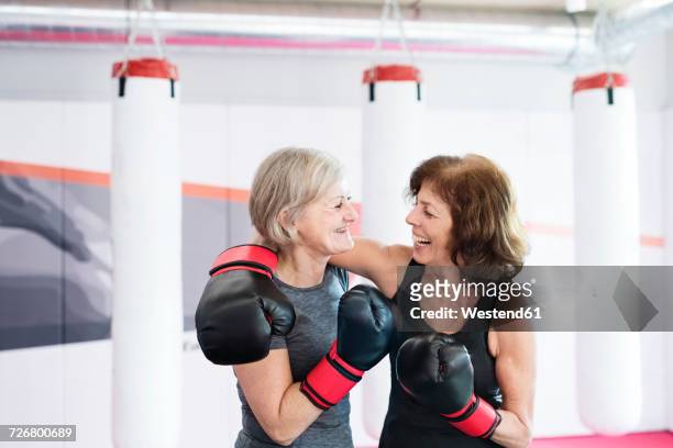 Two happy senior women with boxing gloves embracing in gym