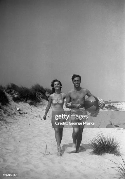 couple walking on beach, man carrying ball, (b&w) - zwart wit vintage stockfoto's en -beelden