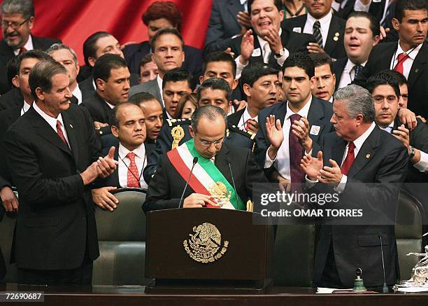 Mexican President Felipe Calderon arranges the presidential sash as outgoing President Vicente Fox and the president of the Chamber of Deputies Jorge...