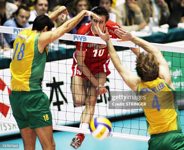 Poland volleyball player Mariusz Wlazly spikes the ball to break the block of Brazil opponents Dante Guimaraes Amaral and Andre Heller of Brazil...