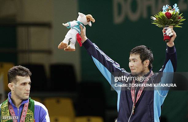 Mongolia's Tsagaanbaatar Haskhbaatar raises his arms in jubilation on a podium as silver medalist, AS Arash Miresmaeili of Iran looks at him after...